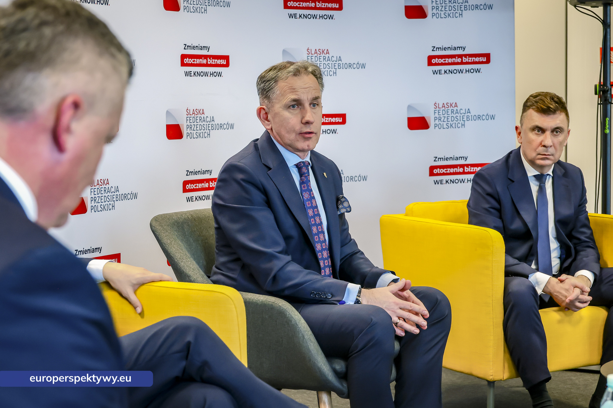 Paneliści słuchają pytania prowadzącego, widok zza jego pleców